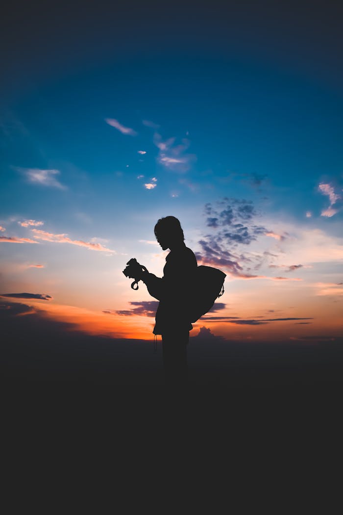 Silhouette of unrecognizable traveler with photo camera at bright sunset